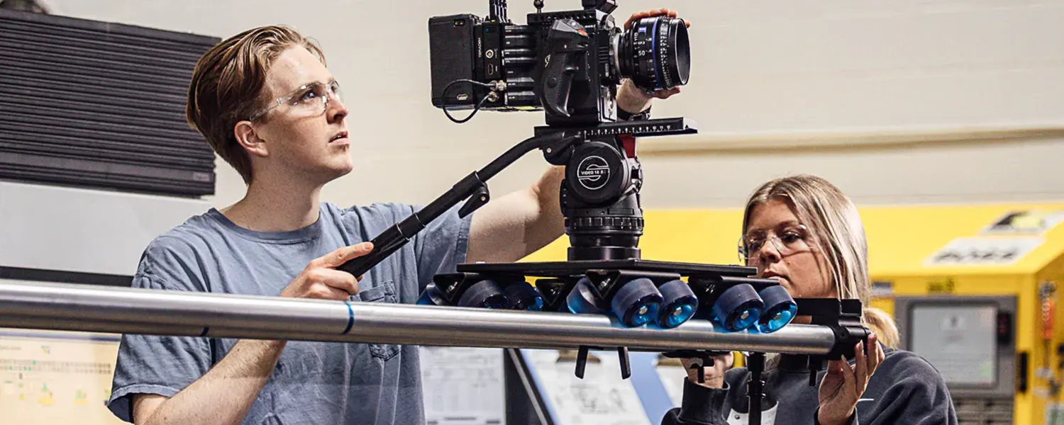 A man and a woman operate a camera on a dolly device.