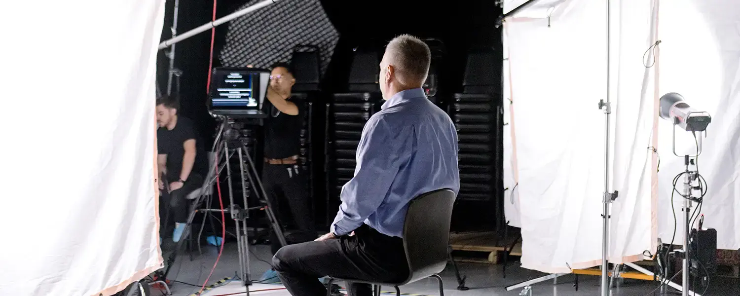 Man sits in lighted studio while being recorded on video